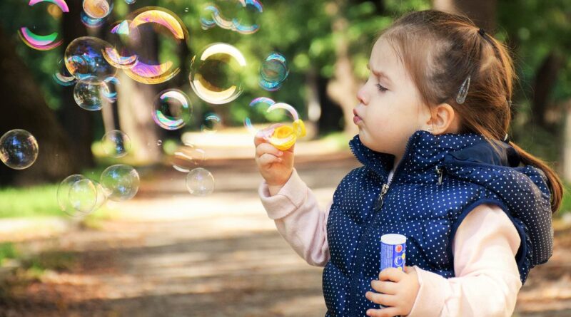 Dziewczynka chodzaca do przedszkola puszcza bańki mydlane w parku
